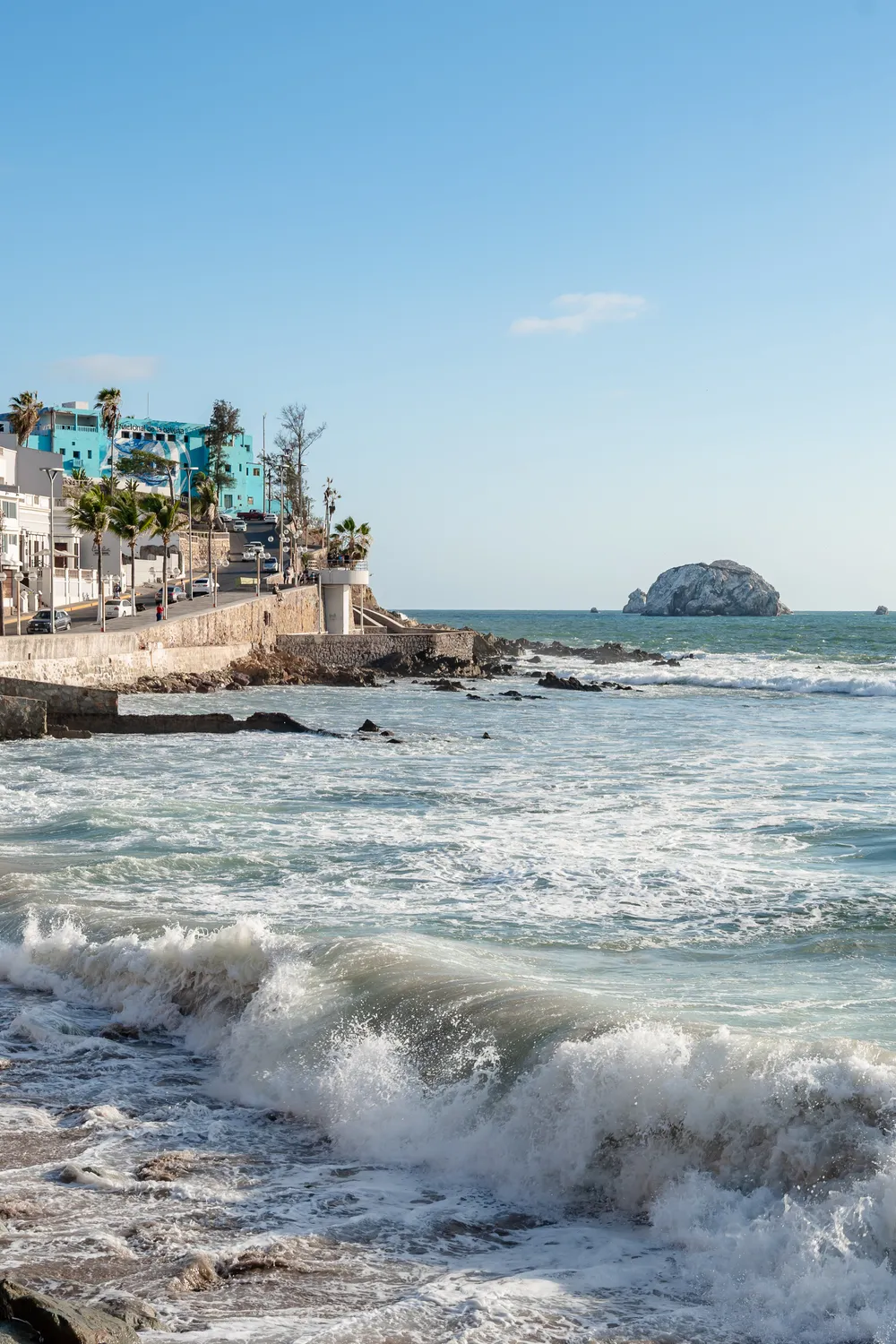 Vertical view of Pacific waves crashing on the rocks in front of the historic Colegio Pacífico building in Mazatlán